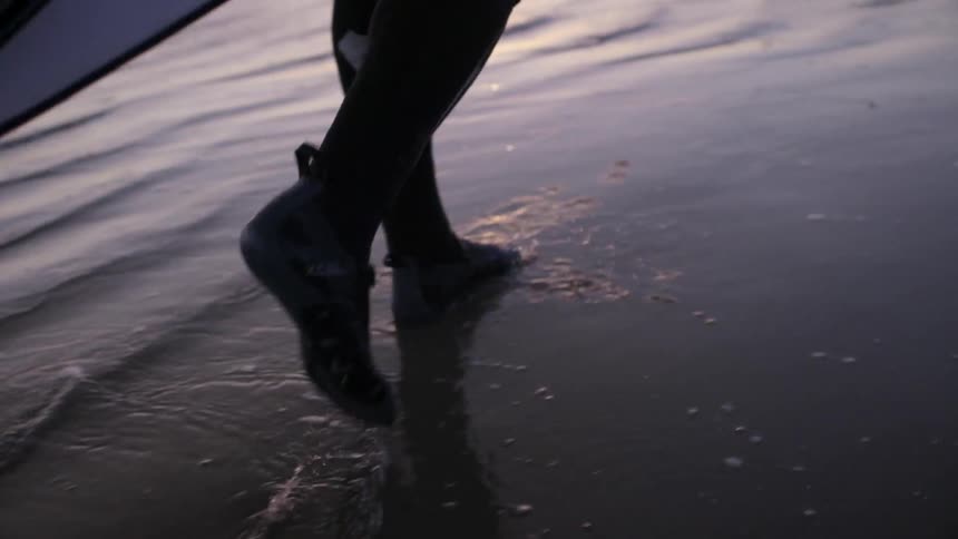 A person walks on the beach in a wet suit