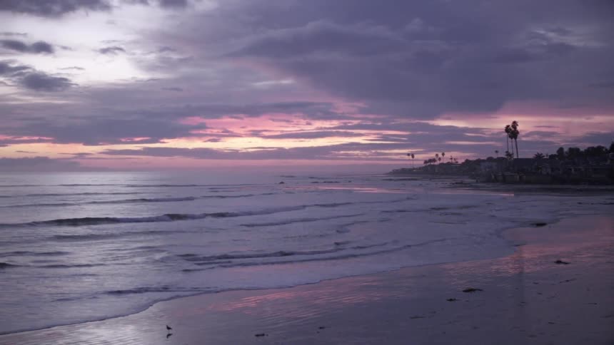 Waves washing ashore as the sun sets in a cloudy sky