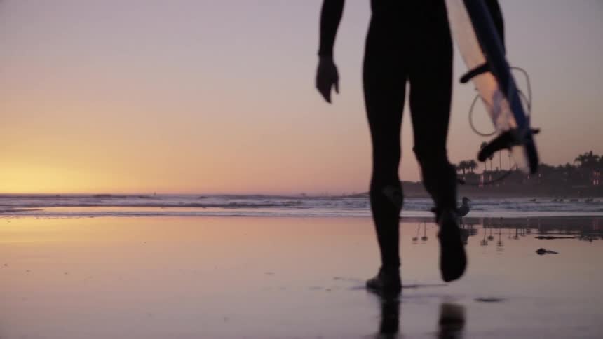 A man is walking along the shore at sunset
