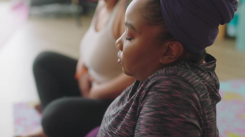 Women sit cross legged deep breathing with their eyes closed as they meditate