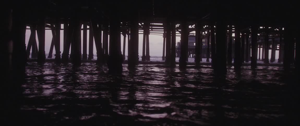 Ocean water swirls around the pylons under a pier
