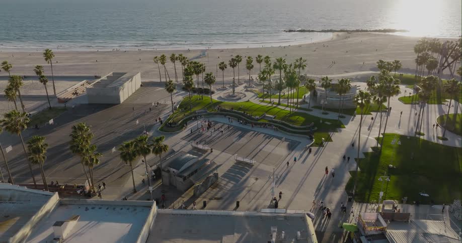 Aerial view of public park with people strolling around next to beach at coastal city at sunset