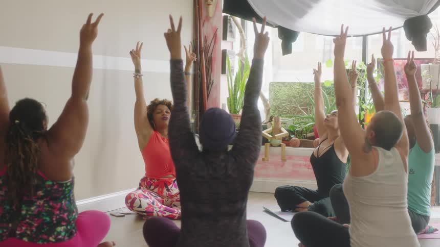 Group of women on a yoga class sitting on yoga mats in a circle in the floor stretching their arms up