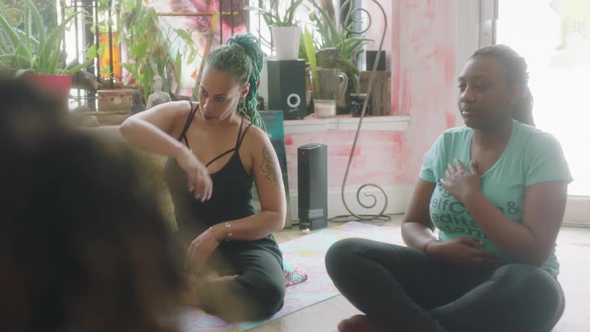Women sit on the floor with their legs crossed and move their arms and shoulders around as they exercise