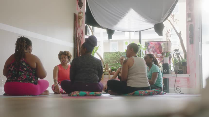 A group of women sit in a circle on small cushions while talking with each other