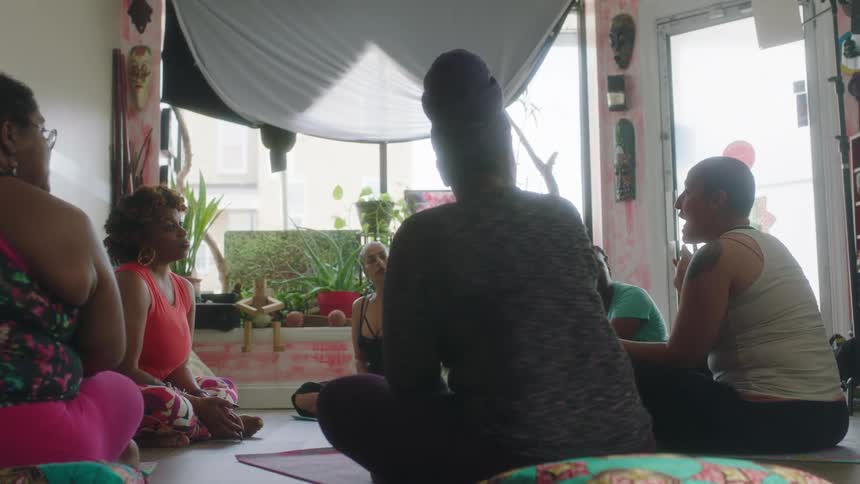 Circle of women sit cross legged on floor while they listen to one talk