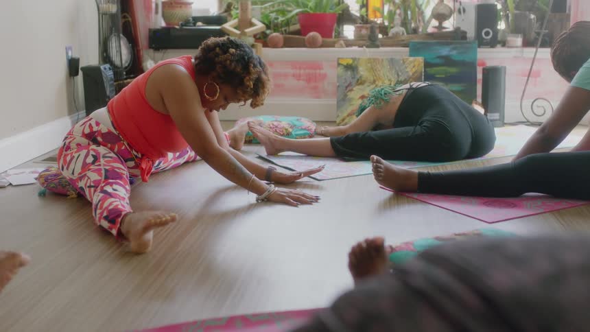 Group of women practice yoga while sitting over mats on the floor of a room