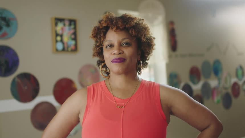 Woman wearing hoop earrings stands with her elbows pointing out in a room with round pictures on the wall
