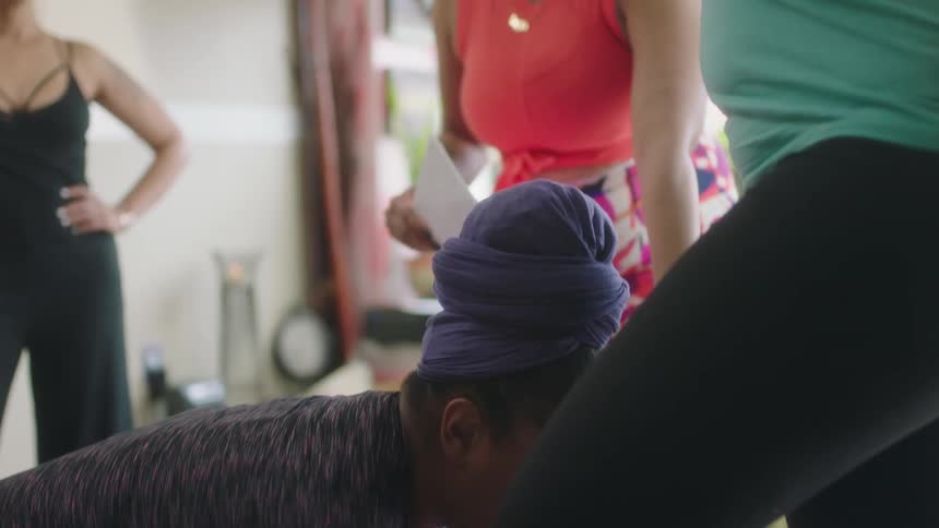 Woman holding a yoga pose surrounded by trainers correcting her pose at home