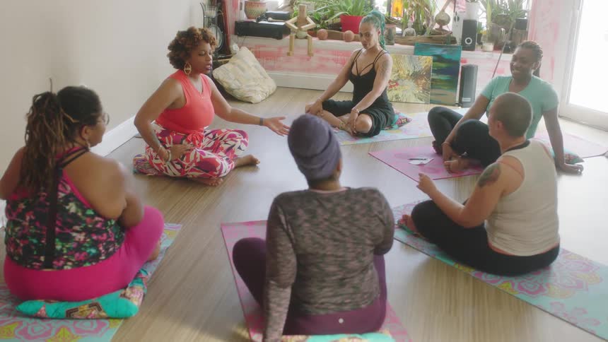 A group of women sitting on yoga mats in a studio talking laughing and sharing