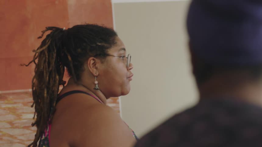 Woman wearing glasses and earrings motions with her hands as she talks while a man sits next to her