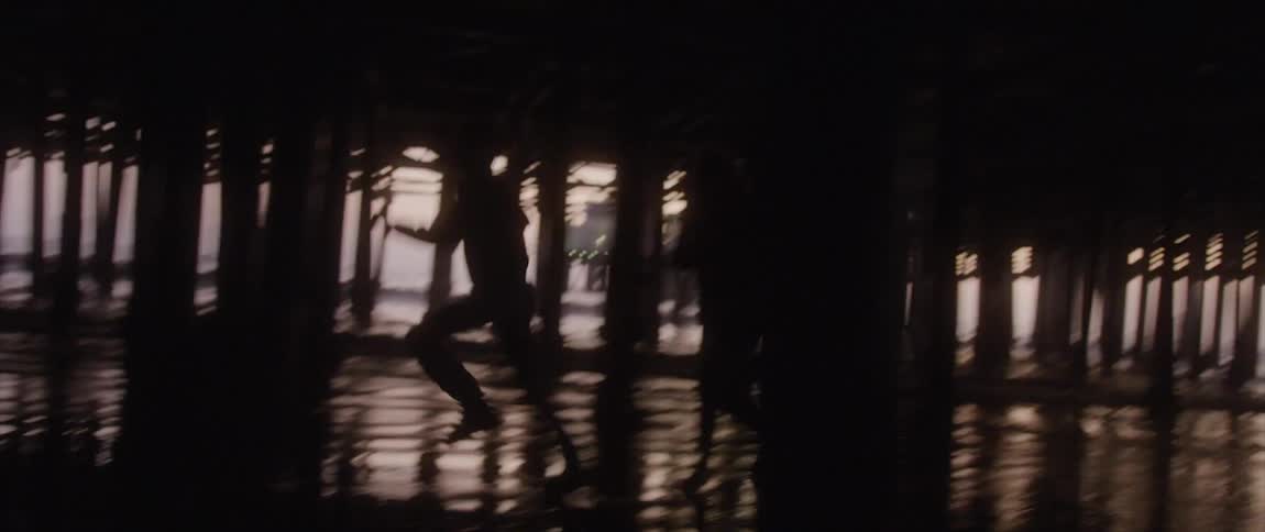 Two people hold hands as they run under the pier in the ocean