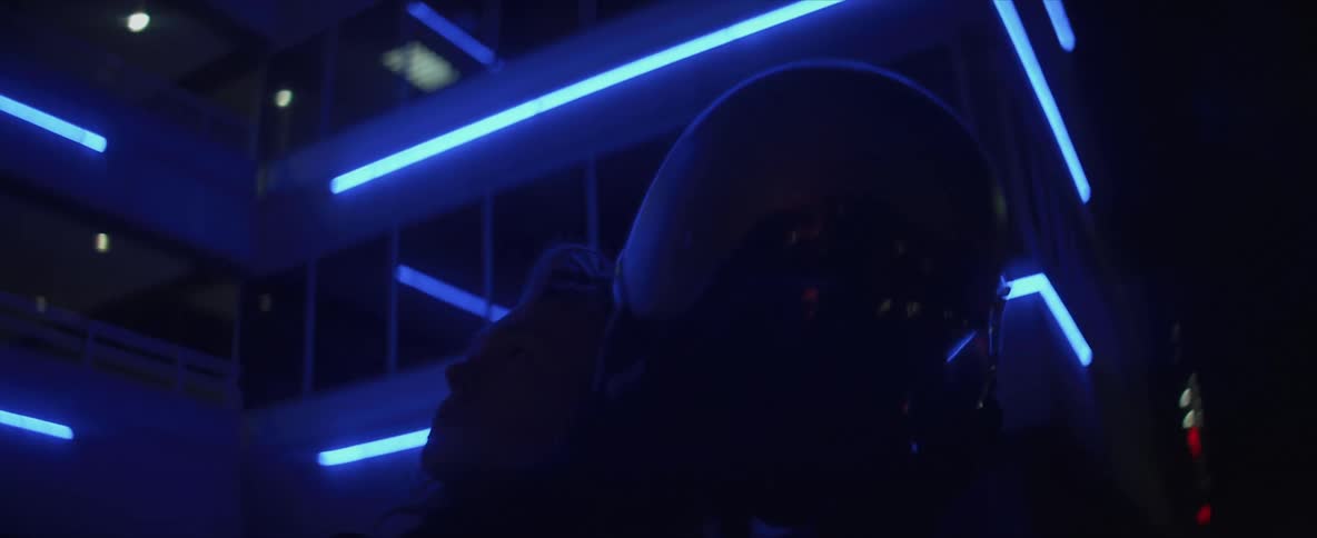 Woman taking off her motorcycle helmet in front of a building illuminated by blue neon lights