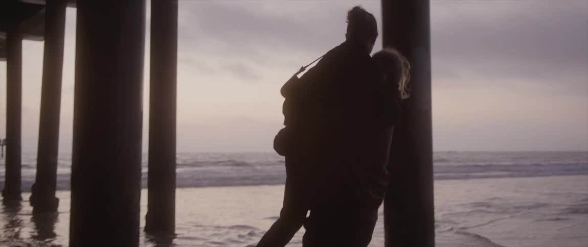 Couple holding each other under pier is silhouetted against the purple sky on the beach