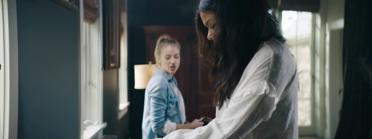 Two female friends chit chat as one looks through records and puts one on to play