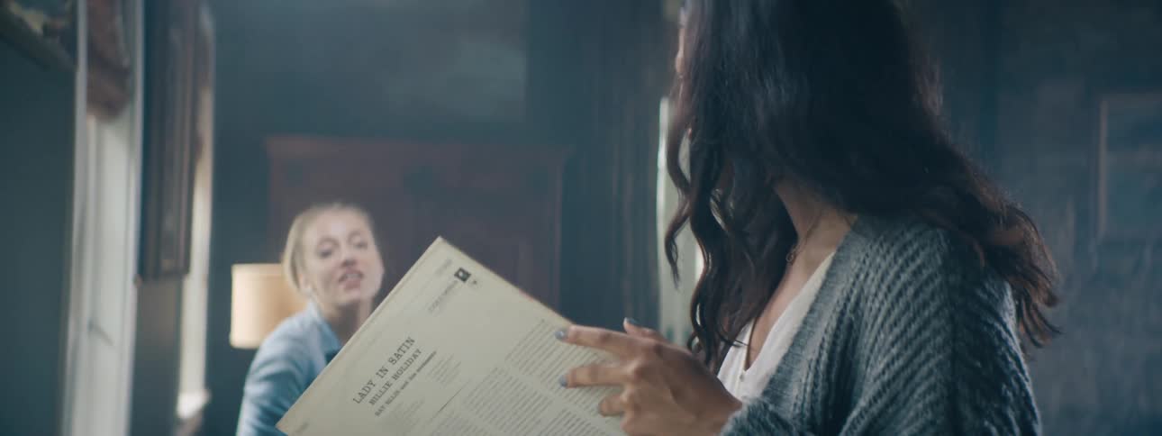 Two young girls hang out and look through records together in a moody library