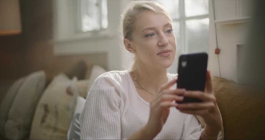 A woman is sitting indoors and looking at her phone