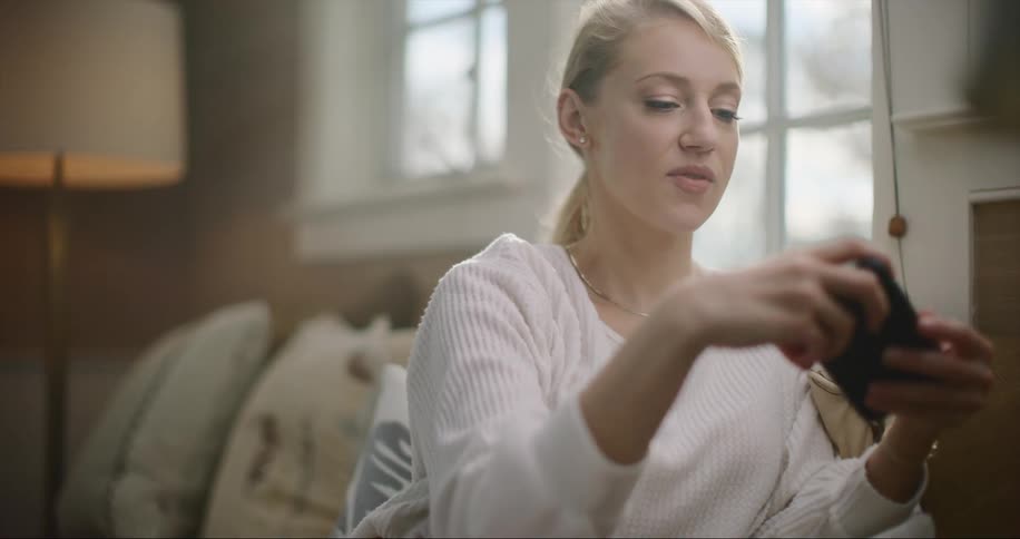 A woman sitting in a living room taps and swipes on her phone turns it and smiles at the screen