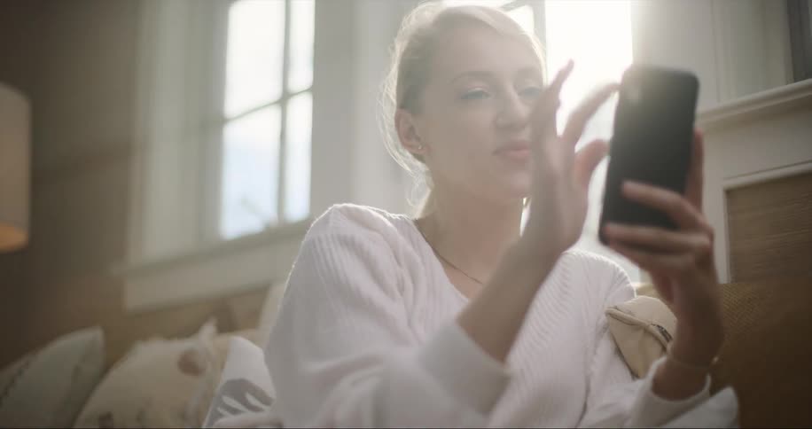 A woman laughs while scrolling through her smartphone on the couch