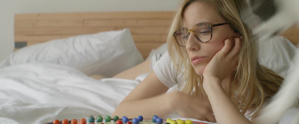 A woman is laying in bed playing a game when the cat jumps in