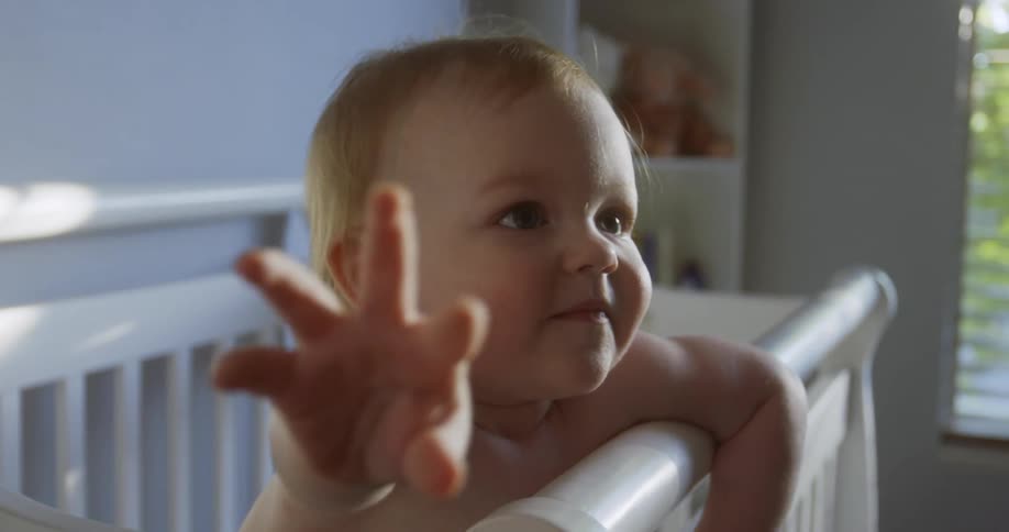 A baby reaches out while standing in its crib