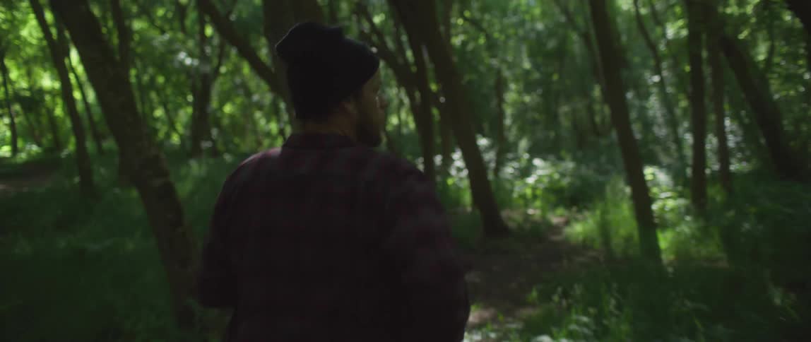 Man wearing a toque and a plaid shirt runs on a path in the forest