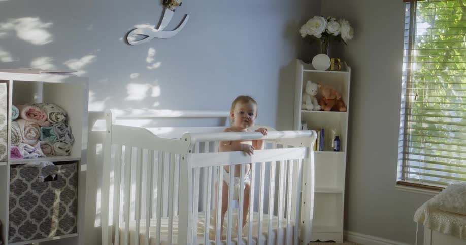 Baby standing at the baby crib in the babys room during daytime