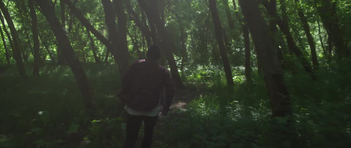 Man wearing wooly hat dark and white shirt and black pants runs away in the green forest