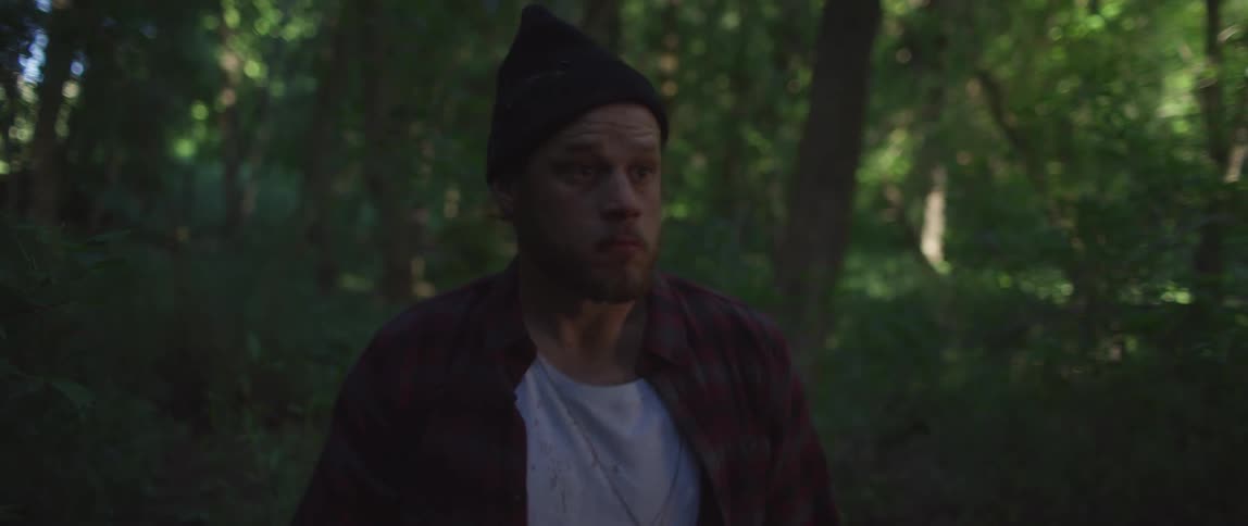 Man wearing a toque looks fearful while in the forest on a sunny day