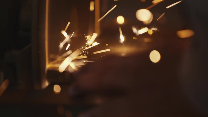 Person holds metal block against spinning disk releasing a shower of sparks