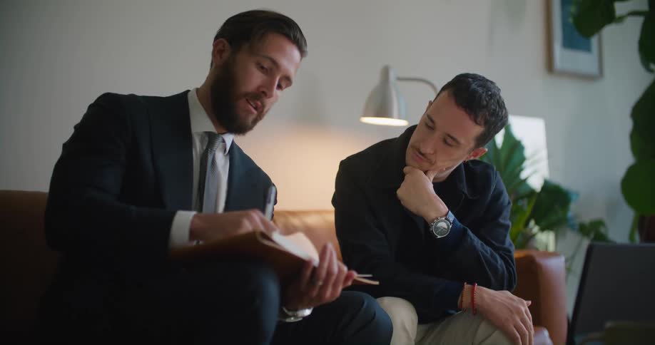 Two men discuss paperwork while sitting on the couch