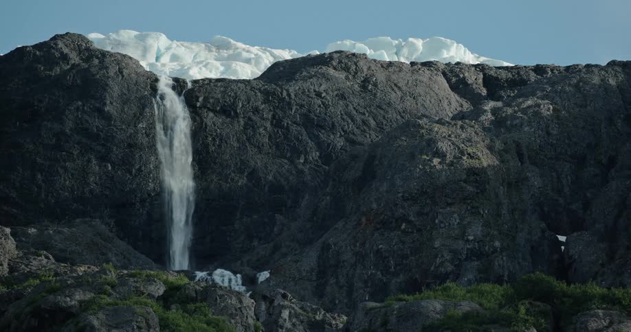 Strong powerful waterfall flowing down the rock face off a mountain glacier in the afternoon