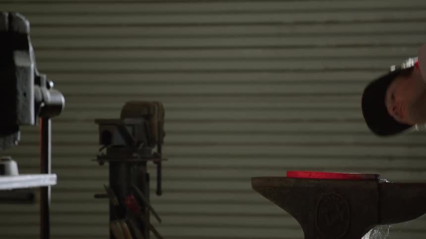 Man uses an anvil to pound on a piece of hot metal then bends over to look at the metal before walking away