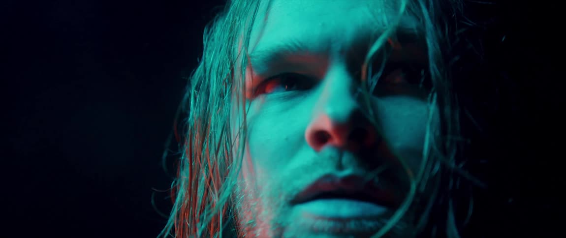 Man with long stringy greasy hair looks to his left