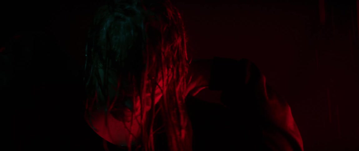 Young strong man with long wet hair under red lights inside a dark room at night