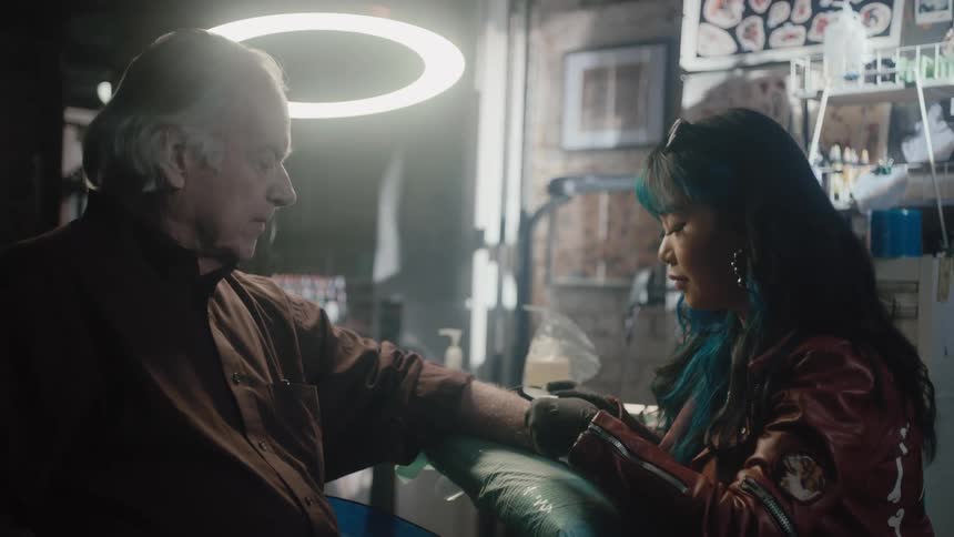 Female tattoo artist puts tattoo on elderly mans arm at tattoo studio