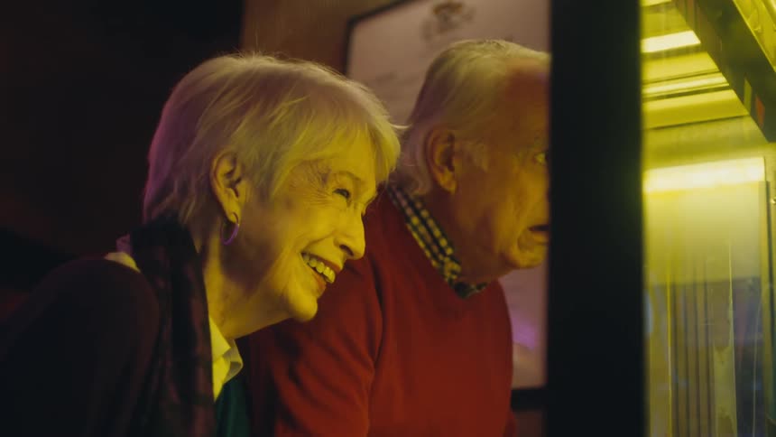 Elderly woman smiles and laughs while an elderly man next to her points to her with his finger