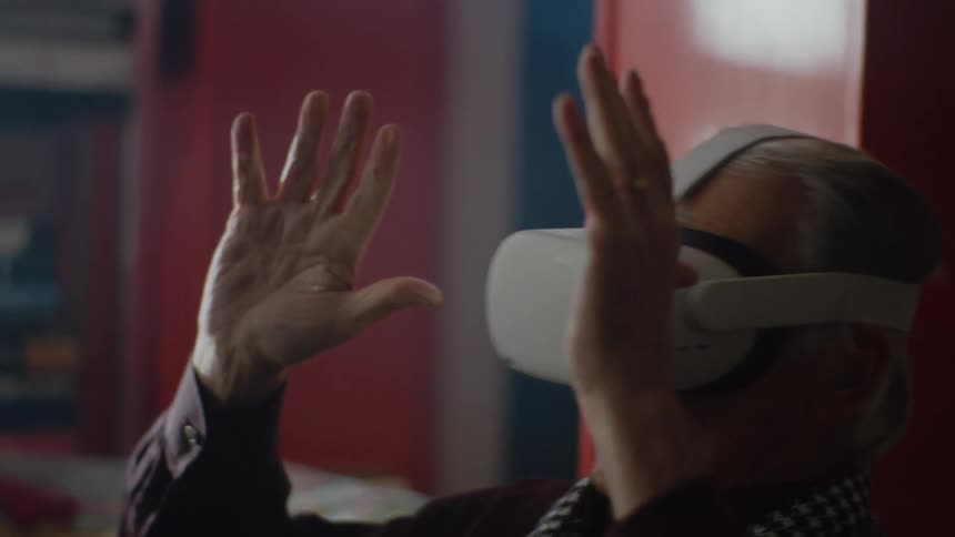 Elderly man sitting on the couch in the living room tries virtual reality goggles