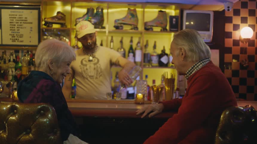 The bartender serves drinks to an elderly couple
