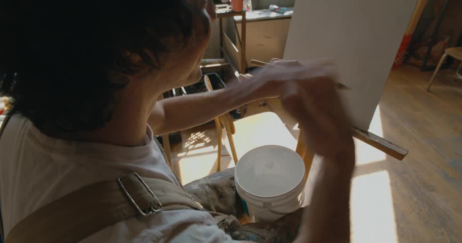 A man is painting on a canvas while sitting indoors