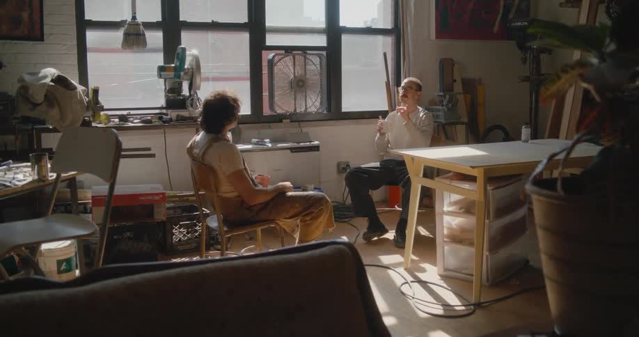 Two men sitting inside a studio talking to each other near a window