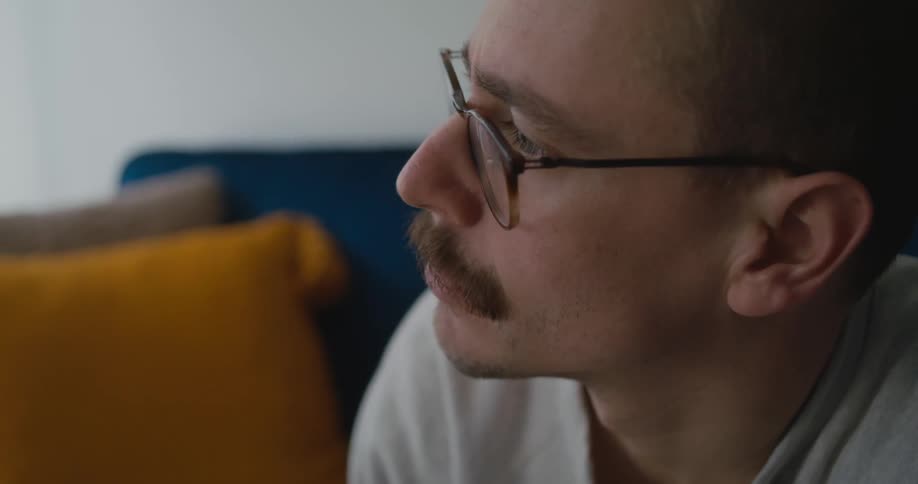 A man drinks from a coffee cup while sitting on a sofa indoors
