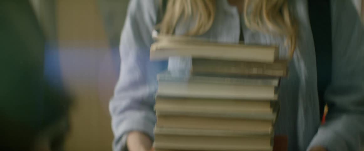 A woman puts a large stack of books on a table