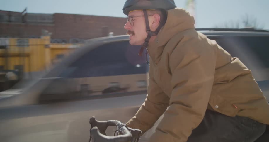 Man with a mustache wears a helmet while riding a bicycle in the city