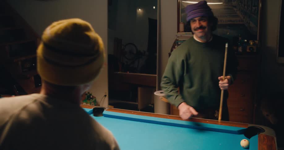 Two men are standing next to a pool table holding cue sticks and they shake hands