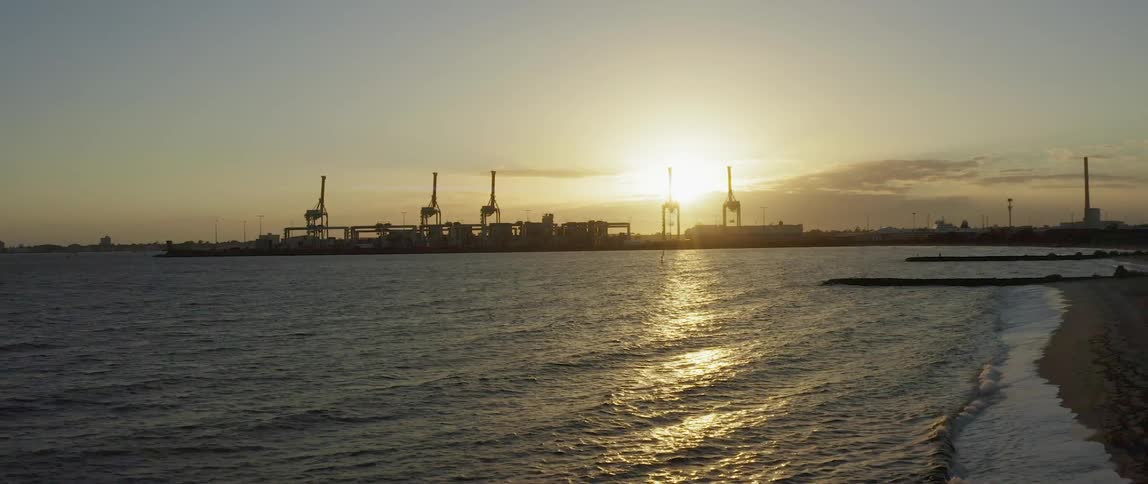 Cranes on docks near beach under rising sun