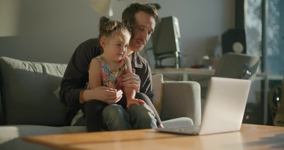 Father and daughter are looking at a laptop and sitting indoors