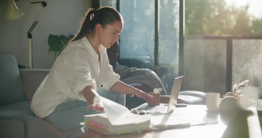 A woman in a room sitting on a couch next to a table and looking at a laptop