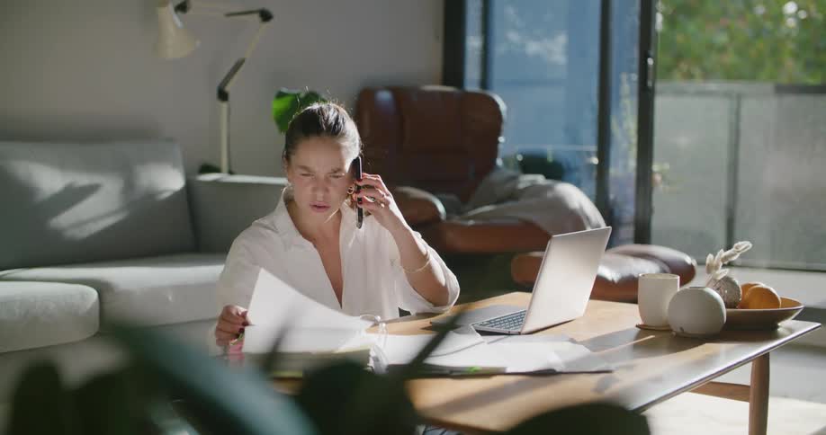Woman sitting in the living room talks on the phone while working