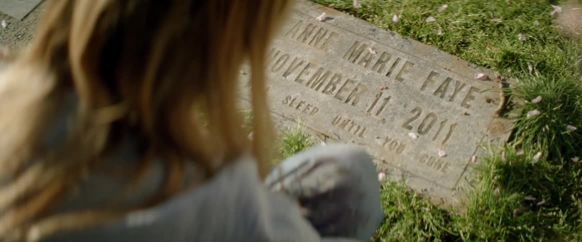 A woman is kneeling before a tombstone